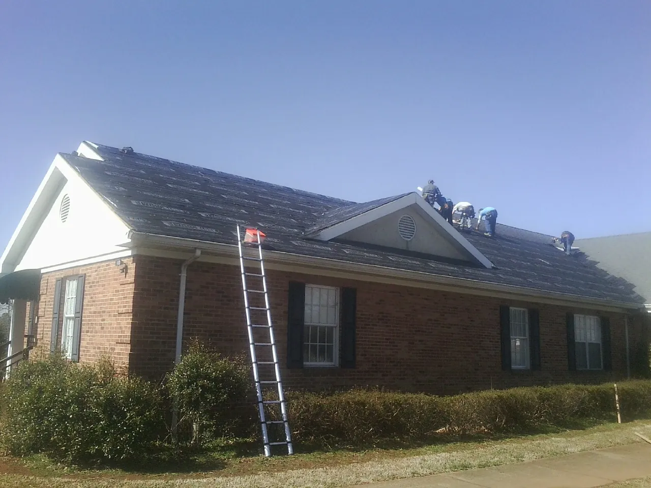 Crew tearing shingles off a brick ranch roof with a ladder set — Emergency Roof Repair work by our crew in New Bloomfield