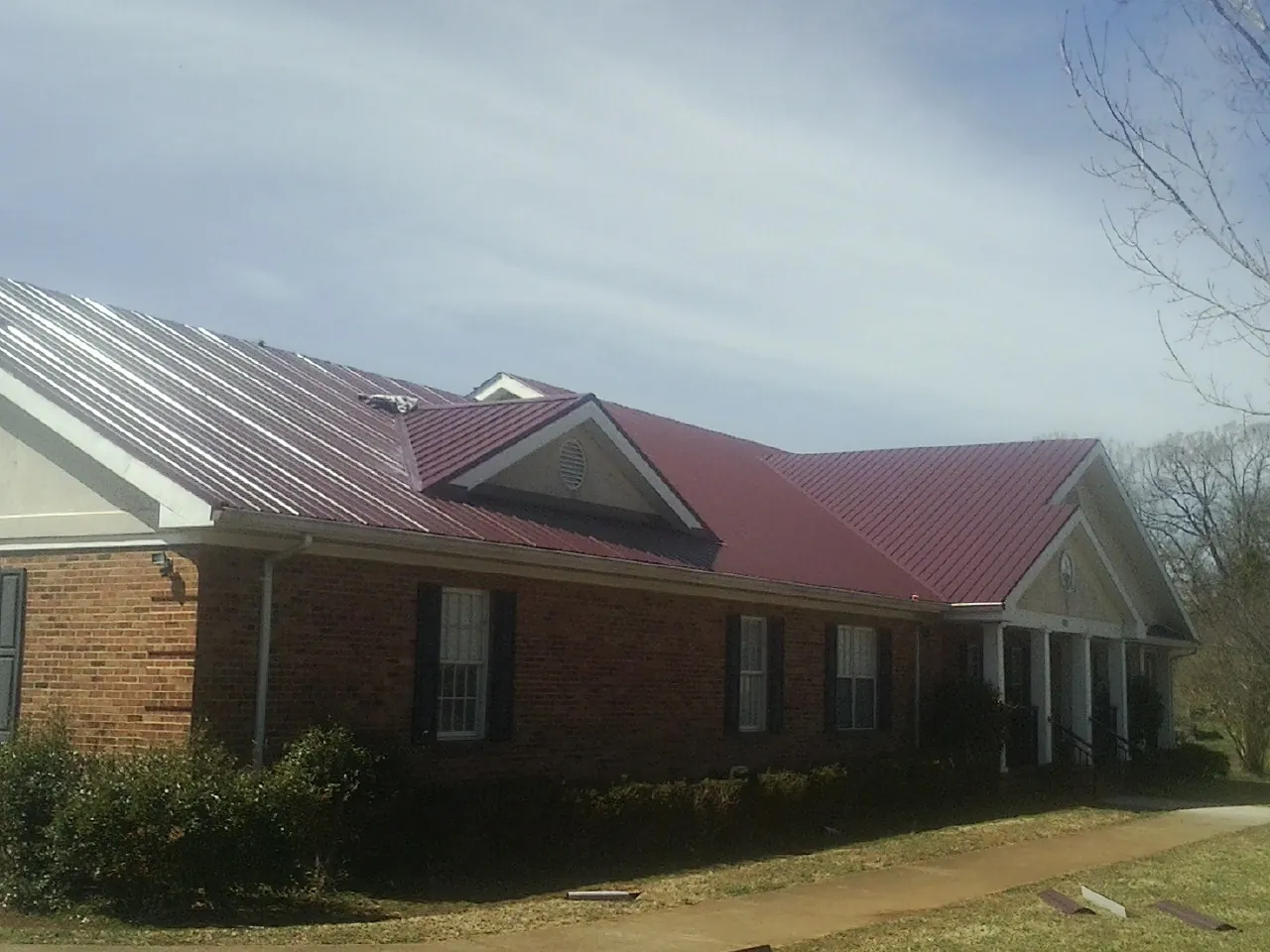 Red metal roof with gabled entries on a long brick building, from a Hail Damage Roof Repair job in New Bloomfield