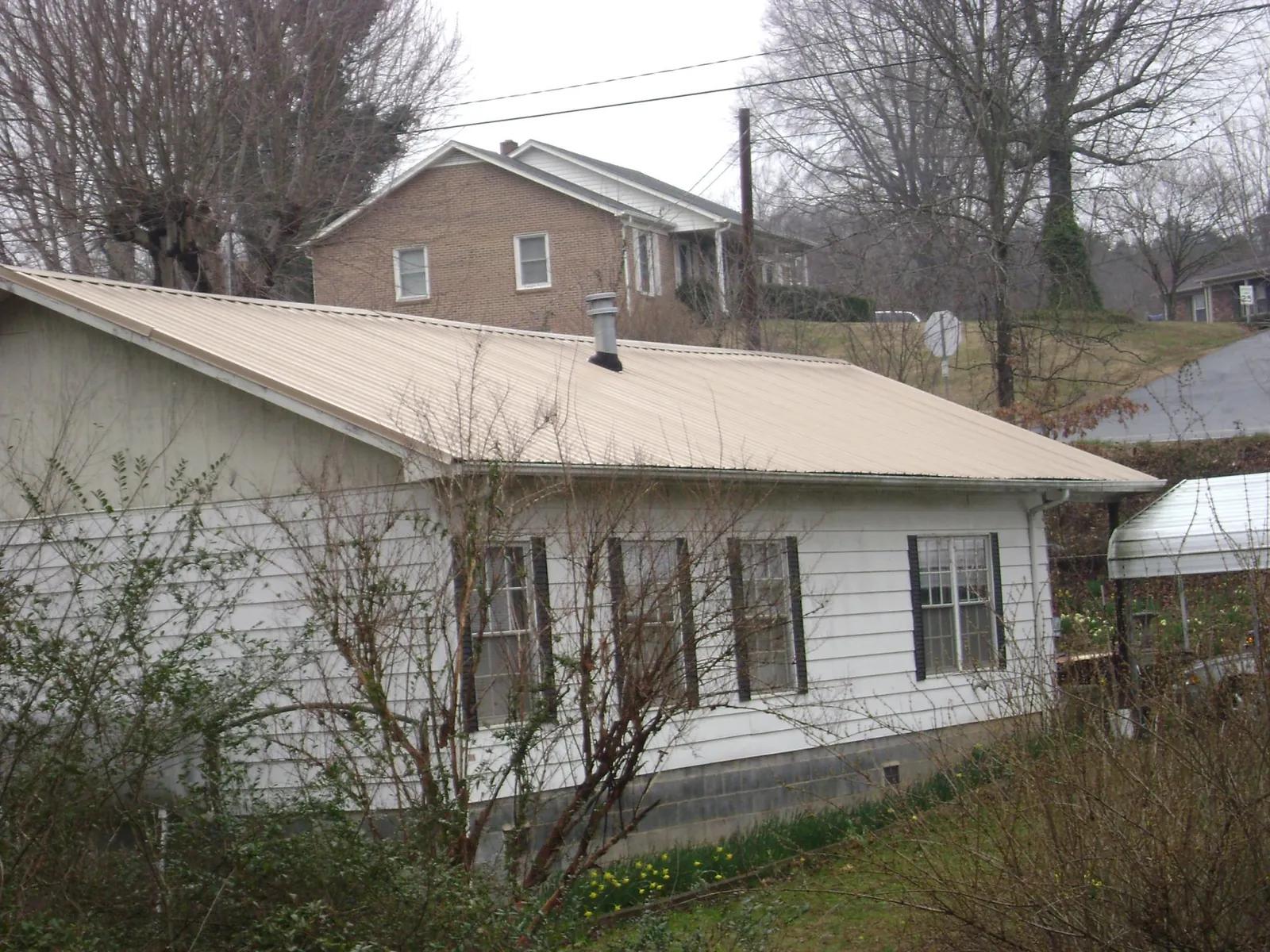 Tan metal roof on a white sided house set into a hillside — Commercial Roofing by Roofing Brothers in New Bloomfield